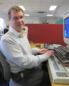 Photo of James Bowden at his desk in the Dolphin Development office, complete with Braille display!