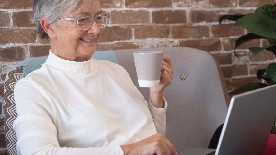 Lady relaxing at home, enjoying reading on her laptop with a cup of tea