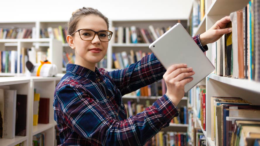 Young student removing a digital tablet from a library shelf.