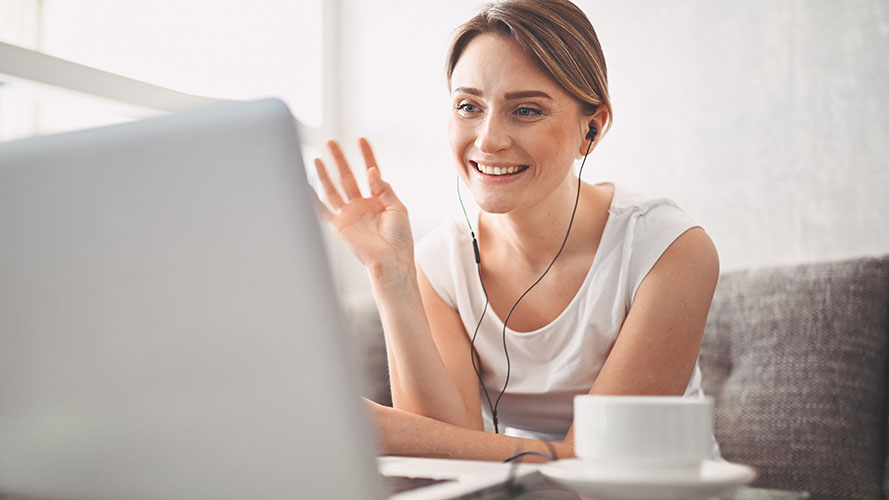 Woman smiling and waving at her laptop screen.