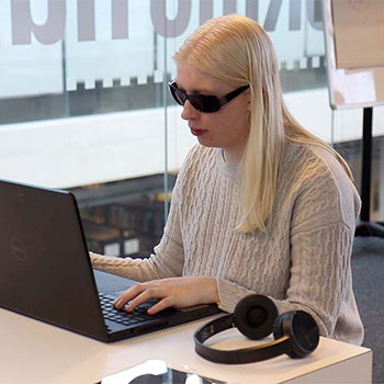 University student wearing dark glasses and reading with her laptop.