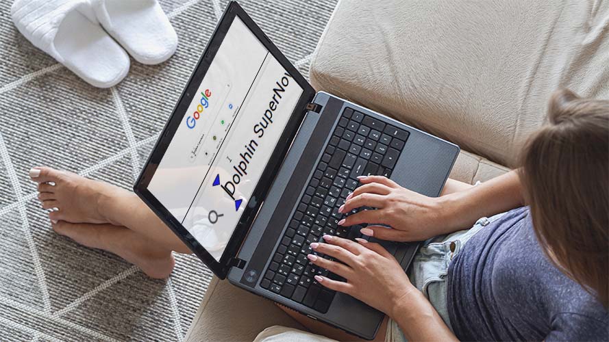 A young woman is relaxing on a sofa and using SuperNova on her laptop.