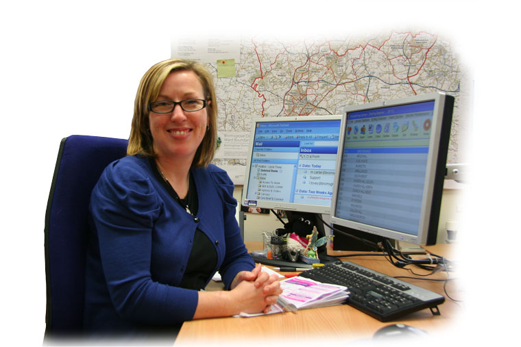 Partially sighted lady sits at a computer with 2 monitors, both showing magnified text.