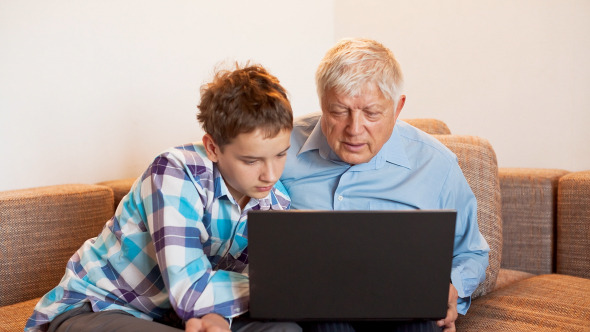 Older man and young boy sitting on a sofa looking at a laptop