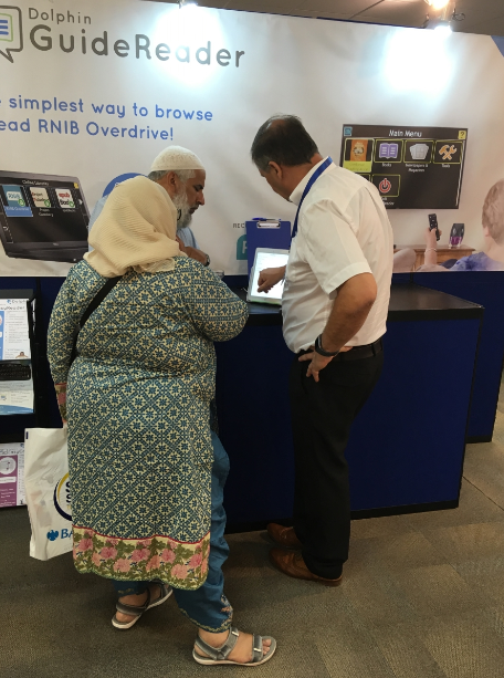 Man in front of Dolphin stand showcasing software on a touchscreen tablet while a man and woman look on